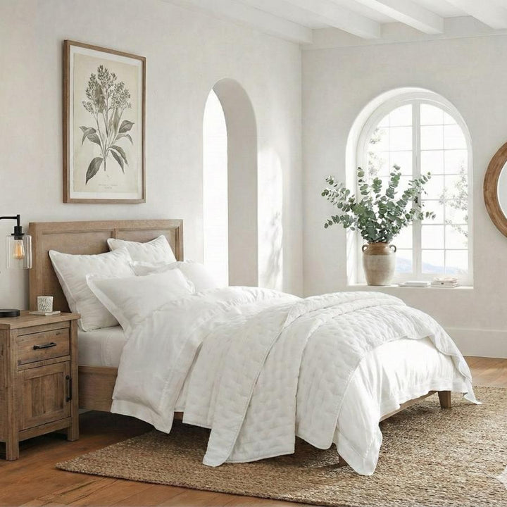 Neatly made bed with white bedding in a bright bedroom with wooden furniture and decorative elements.